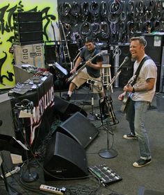 two men are playing instruments in a room full of guitars and other musical equipment on the floor