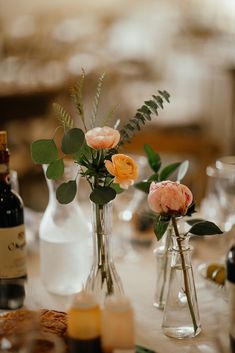 two vases with flowers are sitting on a table next to wine bottles and candles