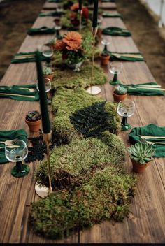 a long table covered in moss with place settings and candles on the top, surrounded by potted succulents