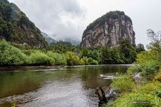 a river with mountains in the background and trees on both sides, surrounded by greenery