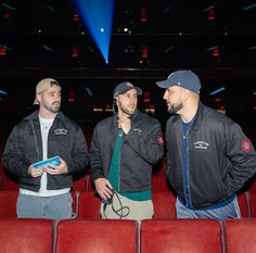 three men are standing in the middle of a theater and one is holding a cell phone