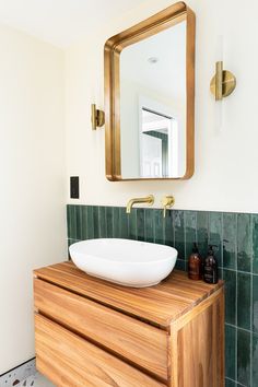 a bathroom with a sink, mirror and green tiled walls in the background is a wooden cabinet