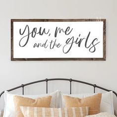 a bed with pillows and a sign above it that says you me and the girls