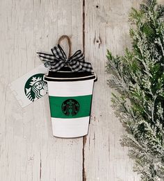 a starbucks cup with a black and white bow on it next to a christmas tree