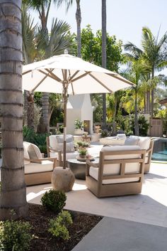 an outdoor patio with furniture and umbrellas near a swimming pool, palm trees in the background