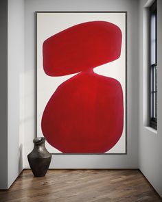 an abstract painting hangs in the corner of a room next to a vase and window