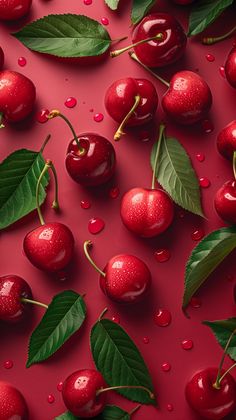 cherries and leaves on a red surface with water droplets all over them, as well as green leaves