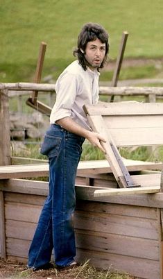 a man standing next to a wooden bench with his hands on the back of it