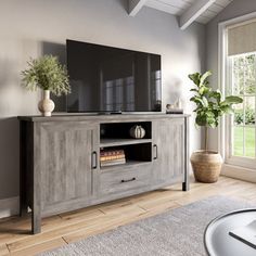 a large flat screen tv sitting on top of a wooden entertainment center next to a window