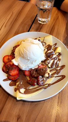 a white plate topped with strawberries and ice cream on top of a wooden table