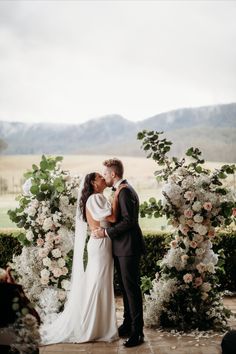 a bride and groom kissing in front of a floral arch