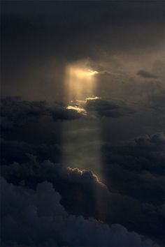 the sky is filled with dark clouds and light shining from behind an object in the distance