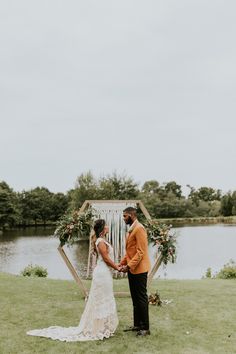 a bride and groom standing next to each other in front of a lake holding hands