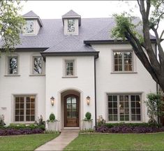 a white house with two story windows and trees in the front yard, surrounded by green grass