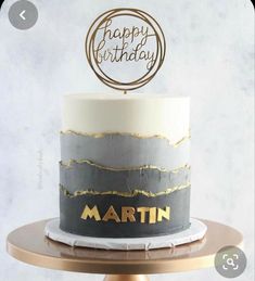 a birthday cake that is decorated with gold and grey frosting on a wooden stand