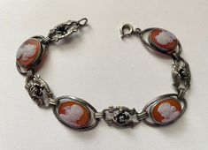 This is a beautiful vintage 900 silver sardonyx cameo link bracelet. Bracelet is hallmarked 900. It features for beautifully carved sardonyx cameos with four beautiful flower and filagree links between. The widest part of the bracelet is 1/2" . The bracelet is 7 1/2" long  This exquisite item is in excellent preowned vintage condition. I have not polished the bracelet to preserve the patina. It will be up to the new owner to decide if they want to polish it or not Silver Cameo Bracelet For Gifts, Vintage Silver Cameo Bracelet, Vintage Intaglio Bracelets For Formal Occasions, Vintage Intaglio Bracelet For Gift, Art Deco Silver Cameo Jewelry, Elegant Silver Bracelet With Cameo, Formal Oval Intaglio Bracelet, Antique Oval Cameo Bracelet, Art Deco Cameo Jewelry For Formal Occasions