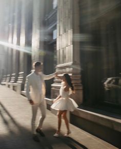 a man and woman walking down a sidewalk next to each other in front of tall buildings