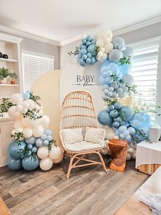 a baby shower with balloons and greenery on the wall next to a wicker chair