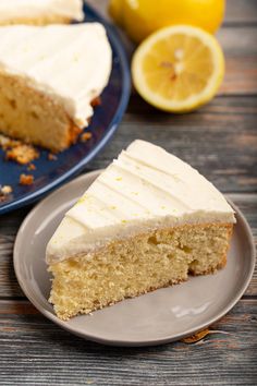 a slice of cake with white frosting on a blue plate next to a lemon wedge