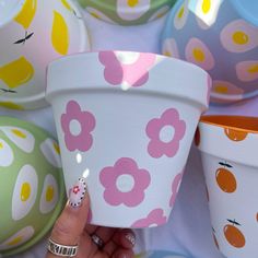 a woman's hand holding up a flower pot with painted flowers on the sides