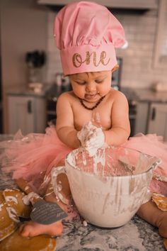 a baby in a pink hat is mixing some icing