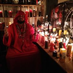 a man sitting in front of candles with his hands up and wearing a red outfit