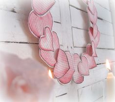 a paper heart wreath hanging on the side of a white brick wall next to two candles