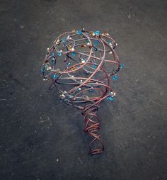 a wire wrapped around a ball on the ground with beads and wires attached to it