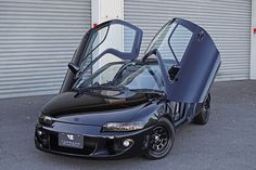 a black car parked in front of a garage with its doors open and the door opened