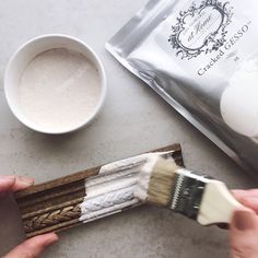 someone is holding a paintbrush and painting the base of a piece of wood next to a cup of coffee