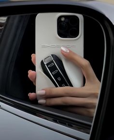 a woman's hand holding a cell phone in front of a car window mirror