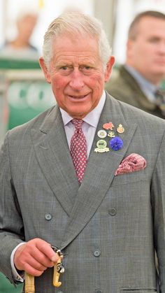 an older man in a suit and tie holding a gold key with other men behind him