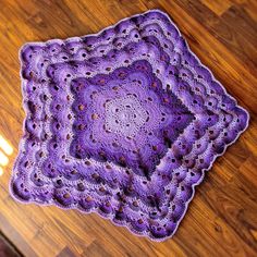 a purple crocheted square sitting on top of a wooden floor