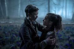 a man and woman standing next to each other in a forest with bluebells