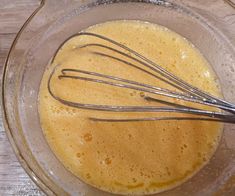 a glass bowl filled with liquid and whisk on top of a wooden table