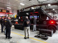 several men are standing in front of a black van with red lights on the side