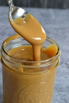 a spoon full of caramel sauce being poured into a jar with the lid open