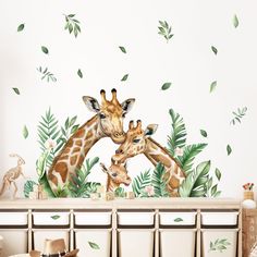 two giraffes standing next to each other with green leaves on the wall