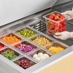 a person is picking up some food from a deli drawer with plastic containers filled with vegetables and other foods