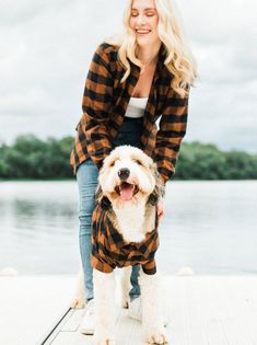 a woman is standing on a dock with her dog wearing a plaid shirt and jeans