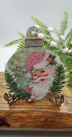 a glass ornament with a santa clause on it's face and green plants