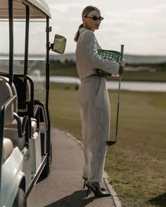 a woman standing next to a golf cart holding a green basket in one hand and wearing sunglasses on the other