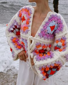 a woman is standing on the beach wearing a crocheted jacket with flowers and hearts