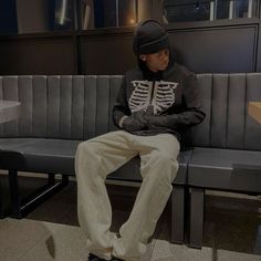 a young man sitting on a bench wearing a skeleton shirt and khaki pants