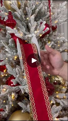 someone is holding a red ribbon in front of a christmas tree