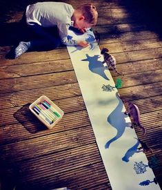 a young boy is painting on a long white paper with dinosaurs and giraffes