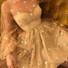 a woman sitting on a couch wearing a dress with gold stars all over the skirt