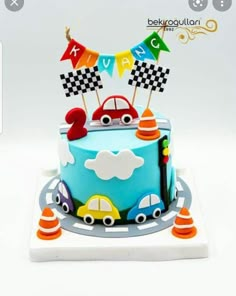 a blue cake with cars and flags on it's top is sitting on a plate