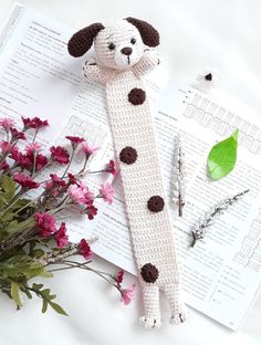 a crocheted dog is sitting on top of an open book next to flowers