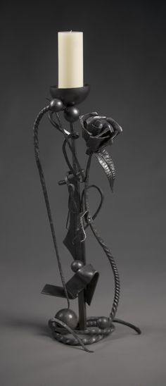 a metal candle holder with a white candle in it's center and an iron rose on top